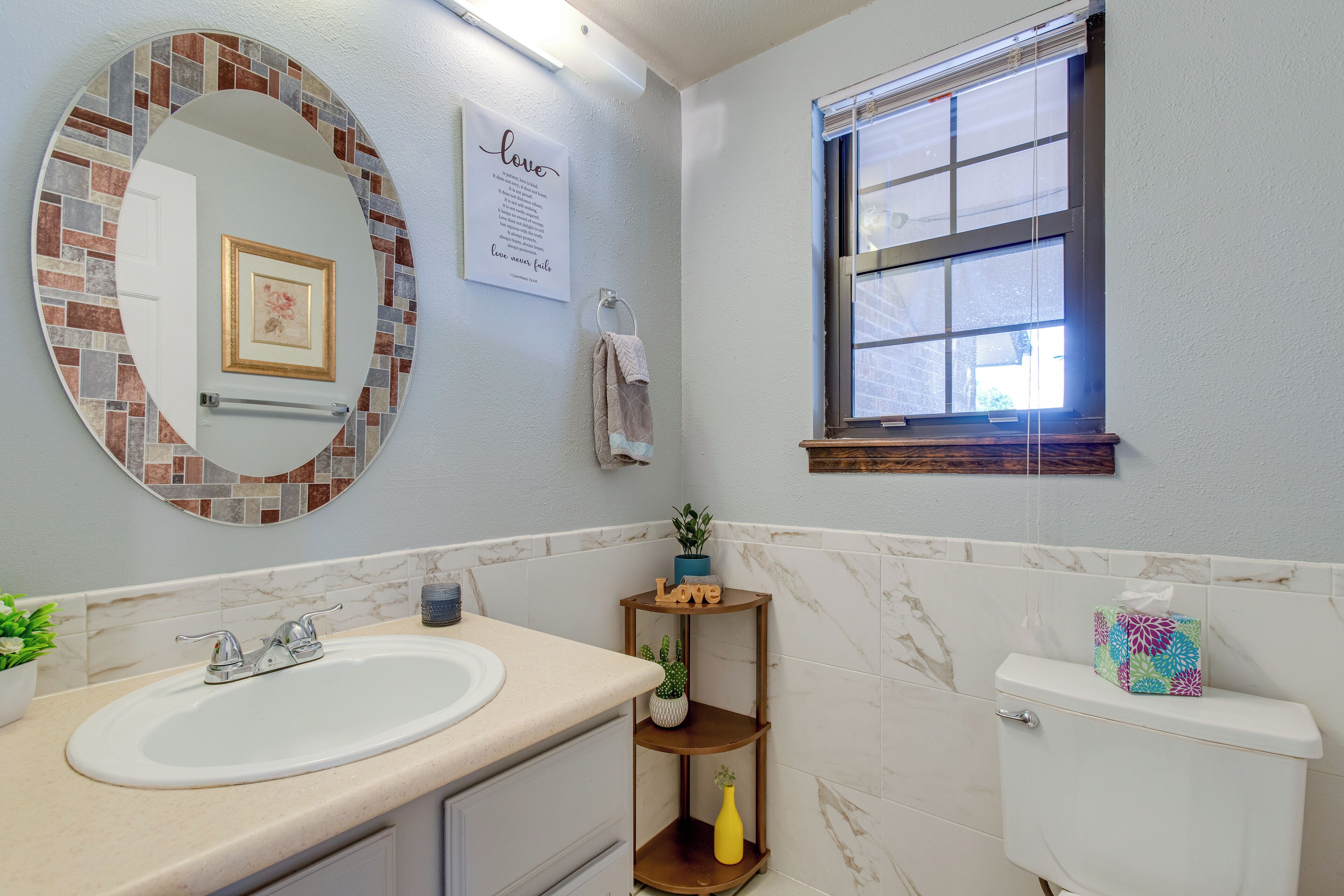 A bathroom with a round mirror, a sink, a toilet, and a window.