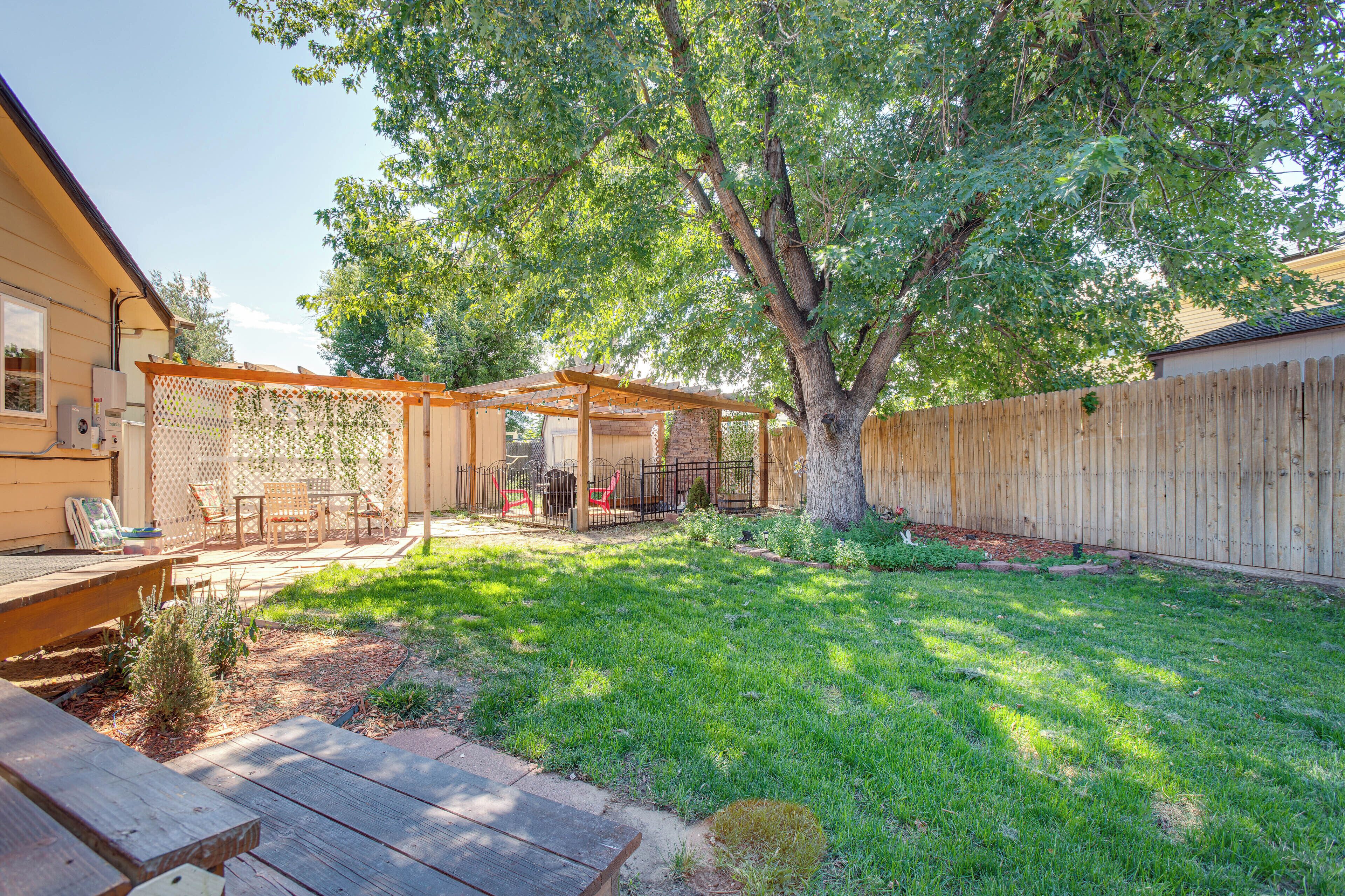 A backyard with a wooden deck, a covered patio area, and a large tree providing shade.