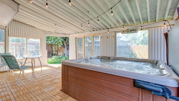 A hot tub in a covered patio area with wooden flooring, a table, and chairs. - Spacious Aurora Retreat w/ Game Room + Hot Tub! (Aurora)