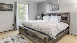 A bedroom with a wooden bed frame, a window with curtains, and a floral painting on the wall. - Spacious Aurora Retreat w/ Game Room + Hot Tub! (Aurora)