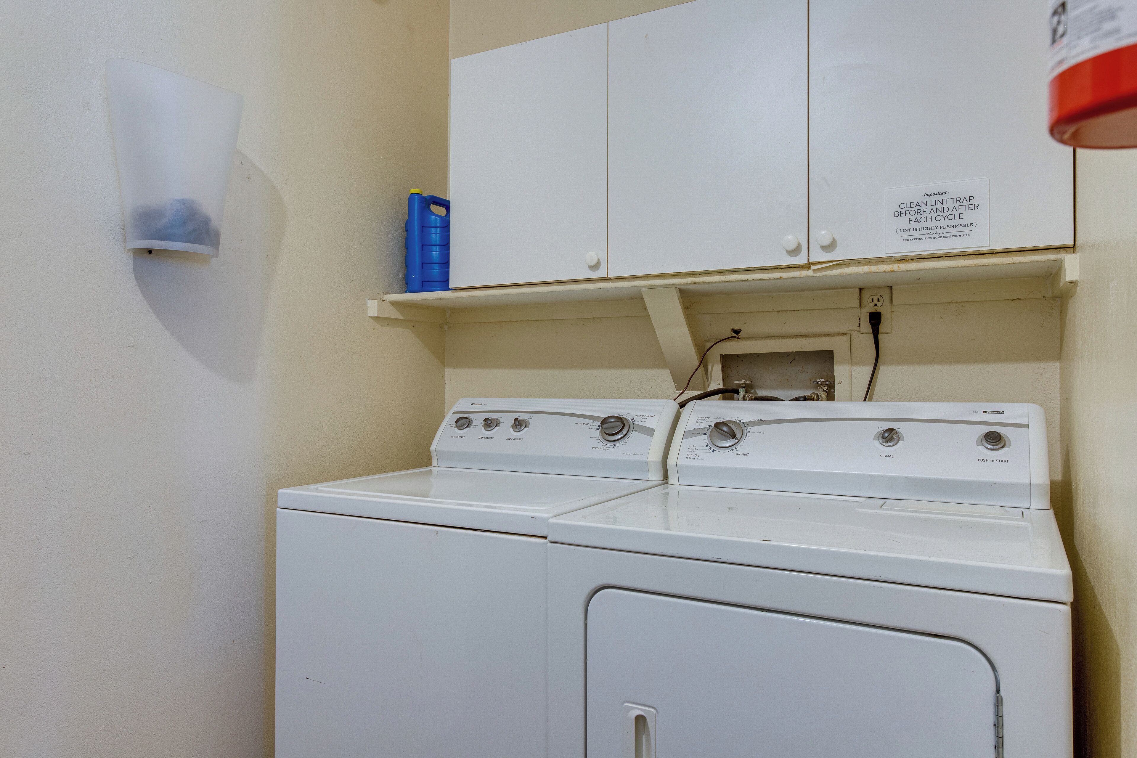 A laundry area with a washing machine and dryer, a white cabinet, and a blue detergent container.