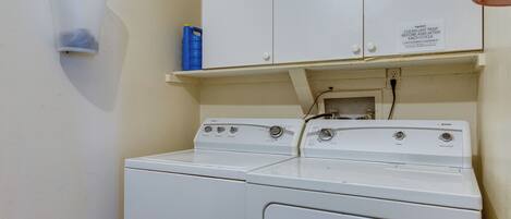A laundry area with a washing machine and dryer, a white cabinet, and a blue detergent container.