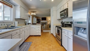A modern kitchen with white cabinetry, stainless steel appliances, and a wooden floor. - Spacious Aurora Retreat w/ Game Room + Hot Tub! (Aurora)