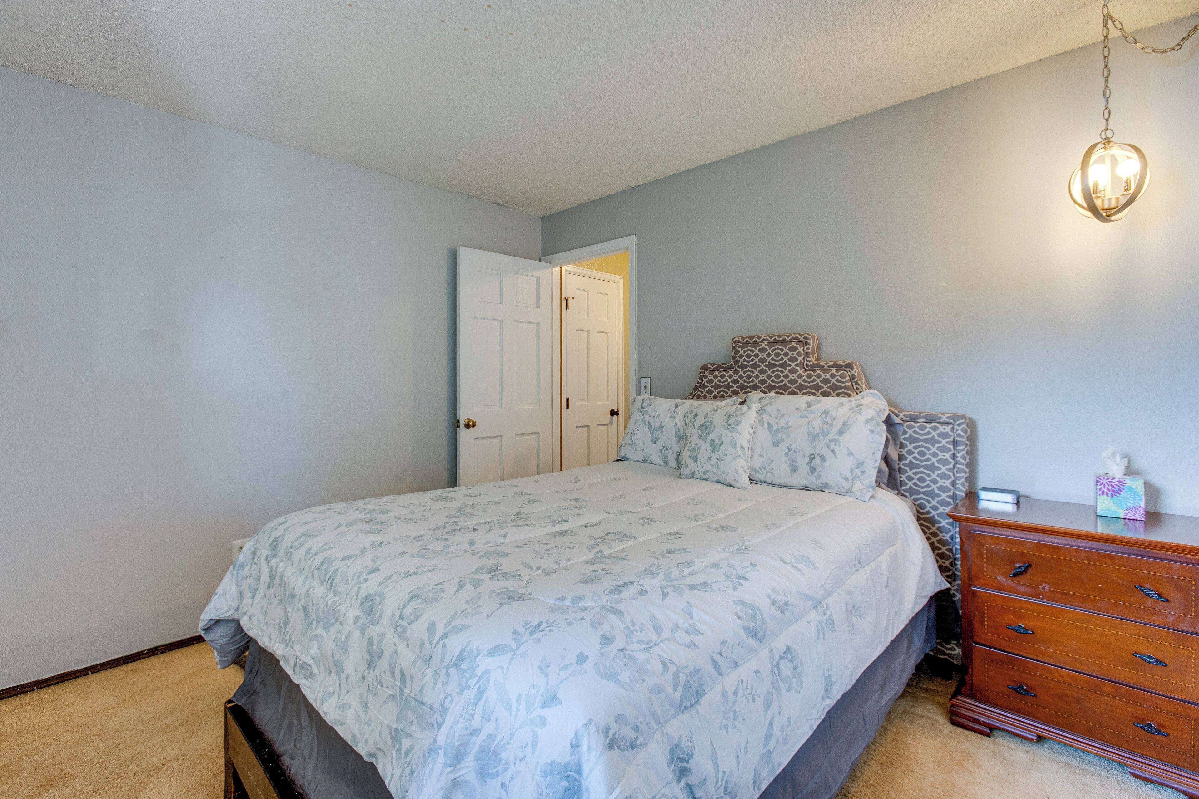 Un dormitorio con cama, cómoda y lámpara colgante.