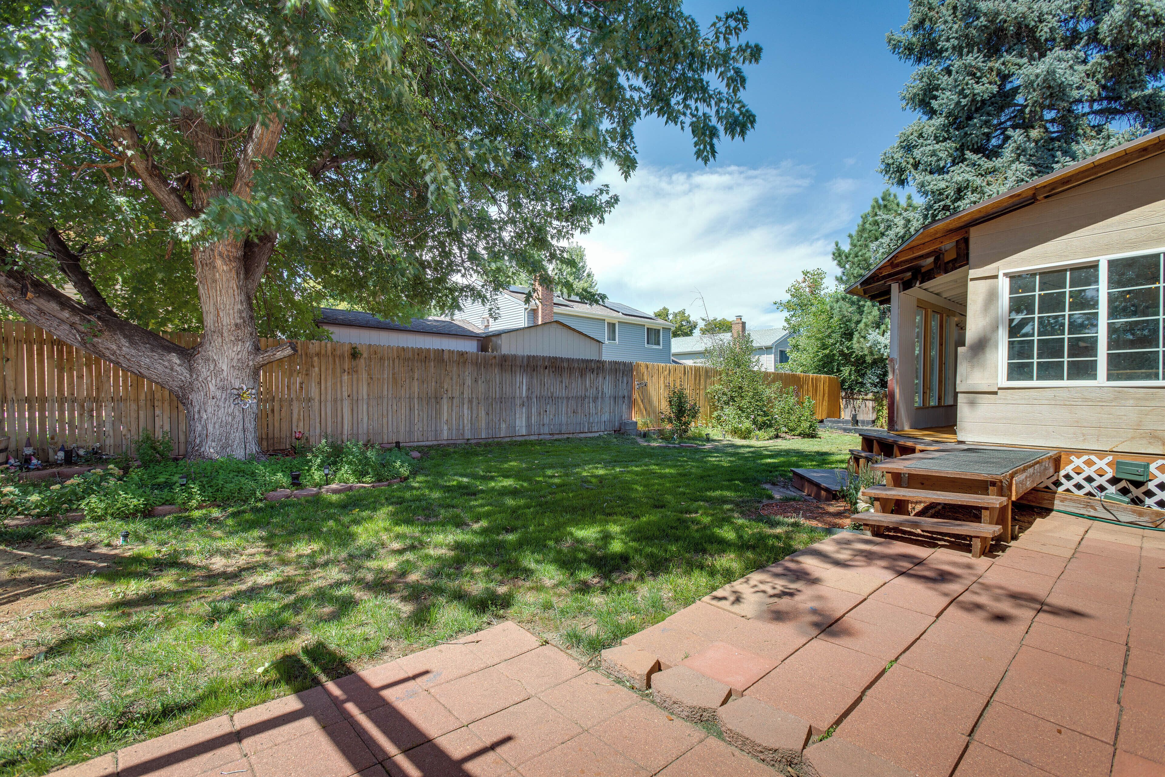 A backyard with a wooden deck, a picnic table, and a large tree.