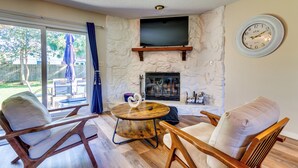 Un salón con pared de piedra, chimenea, televisor y dos sillas de madera con cojines.