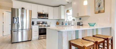 A modern kitchen with white cabinets, stainless steel appliances, a large island with bar stools, and a hanging pendant light.