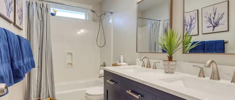 A bathroom with a bathtub, toilet, and a shower. There are towels hanging on the wall and a plant on the counter.