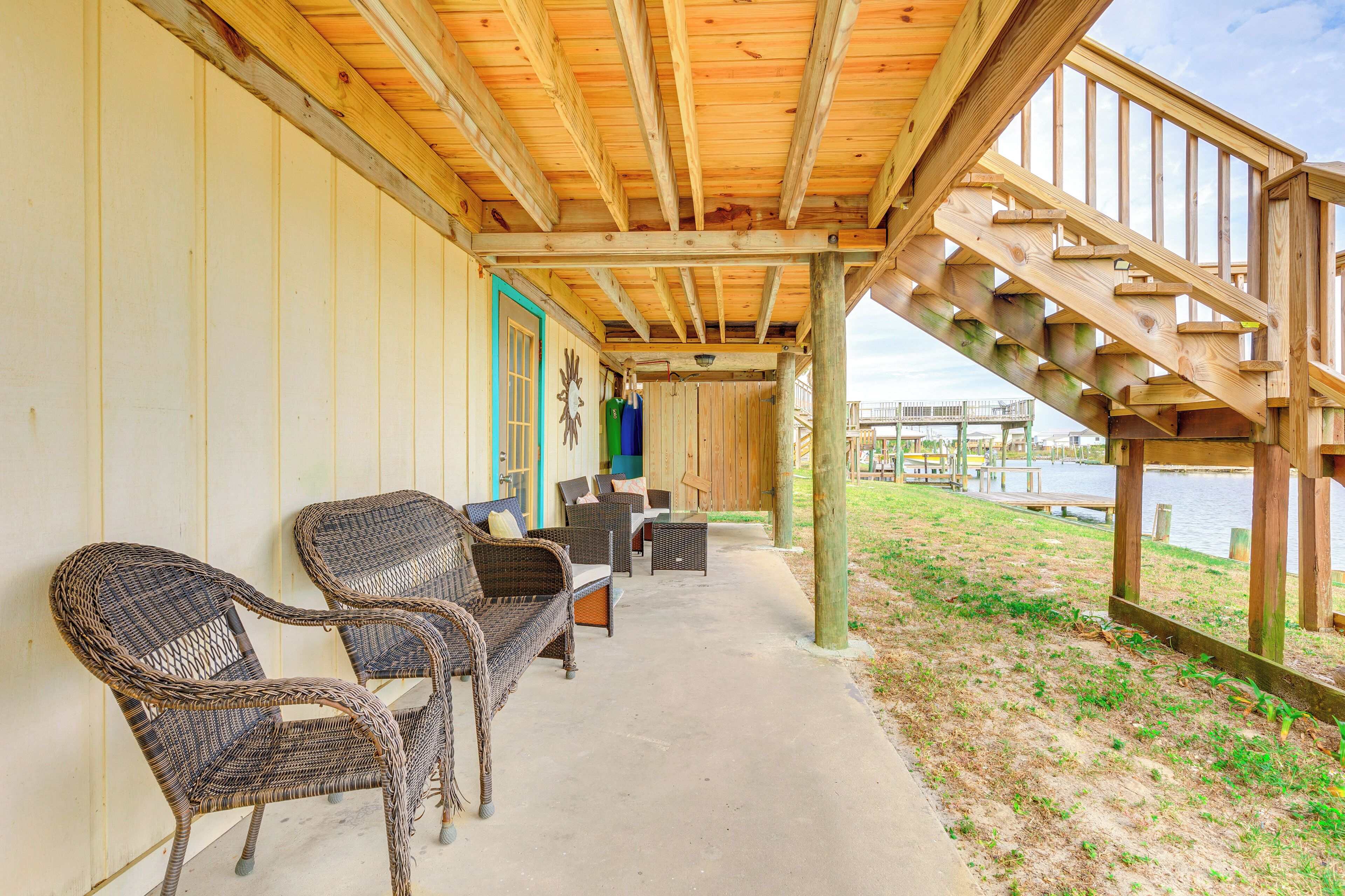 A covered outdoor seating area with wicker furniture and a wooden staircase leading to a dock.