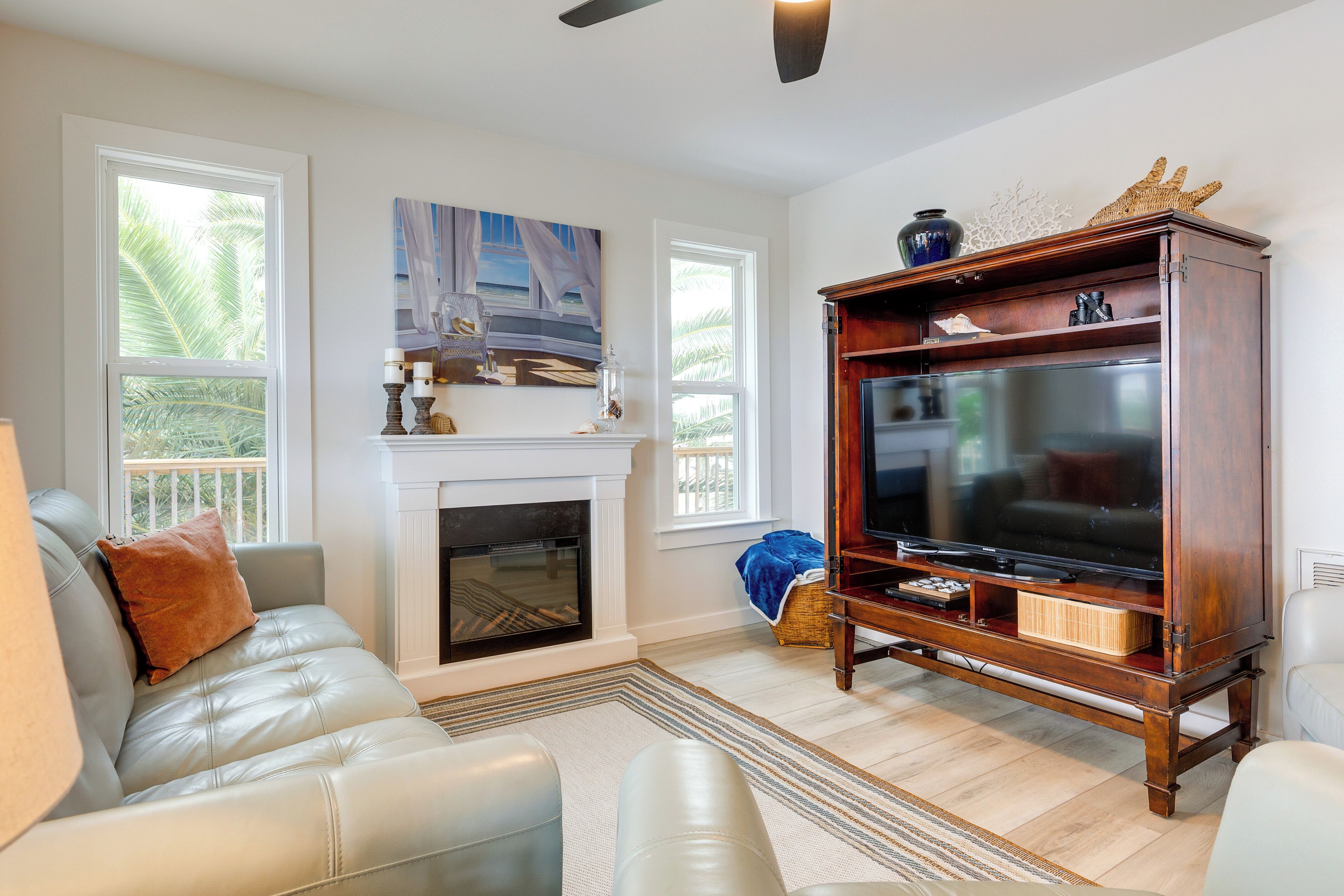 A living room with a fireplace, leather sofa, wooden entertainment center, and large windows.