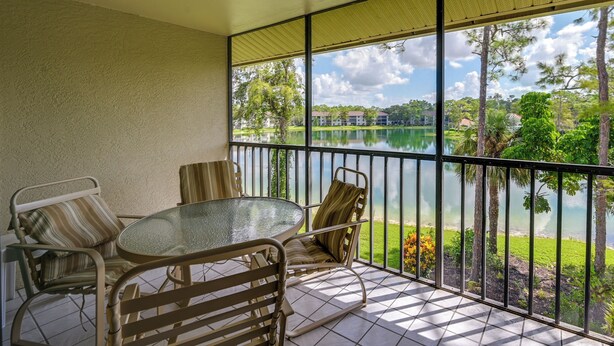 A balcony with a glass table and chairs, overlooking a lake and greenery. - 3 Mi to Beaches: Naples Condo w/ Pool Access! (Naples)
