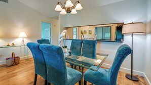 A dining area with a glass table and blue velvet chairs, a chandelier, and a floor lamp. - 3 Mi to Beaches: Naples Condo w/ Pool Access! (Naples)