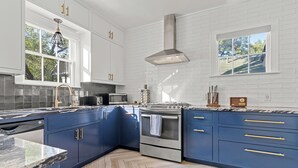 A modern kitchen with white brick walls, blue cabinets, and a stainless steel range hood. - 2 Mi to Downtown Austin: Family Home w/ Porch! (Austin)