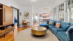 A modern living room with a blue sofa, a wooden coffee table, and a large window. - 2 Mi to Downtown Austin: Family Home w/ Porch! (Austin)