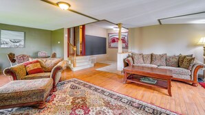 Ein geräumiges Wohnzimmer mit Holzboden, einem großen blumigen Sofa, einem passenden Sessel und einem Couchtisch. Eine Treppe mit roter Wangenverkleidung führt zu einer weiteren Ebene.