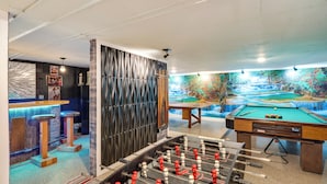 Une table de billard, une table de baby-foot et une table de jeu de fléchettes se trouvent dans une pièce ornée d’une fresque représentant une cascade.