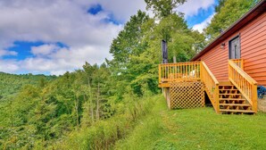 A cabin with a wooden deck and stairs leading to a balcony, surrounded by lush greenery and trees. - Mtn View + Fire Pit: Pet-friendly Woodlawn Cabin! (Woodlawn)