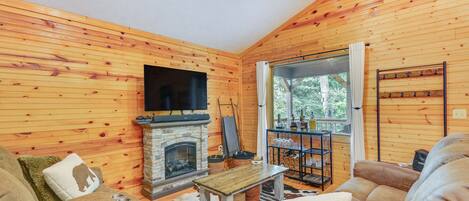 A cozy living room with wooden walls, a fireplace, leather sofas, and a television.