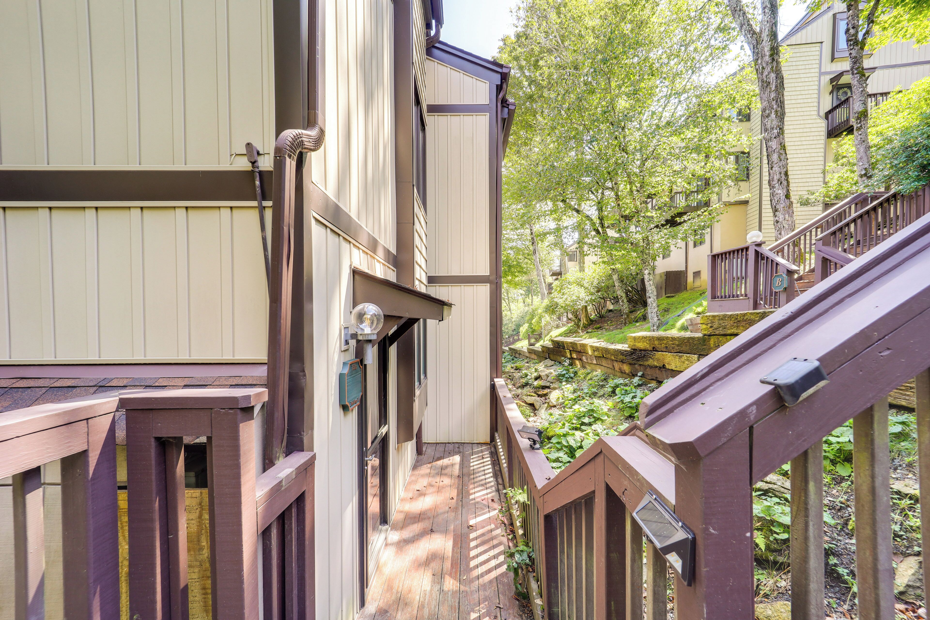 A narrow wooden pathway between buildings with a small garden area and a stone wall.