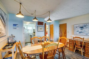 Un comedor con una mesa y sillas de madera, una cocina al fondo y un techo con lámparas colgantes.