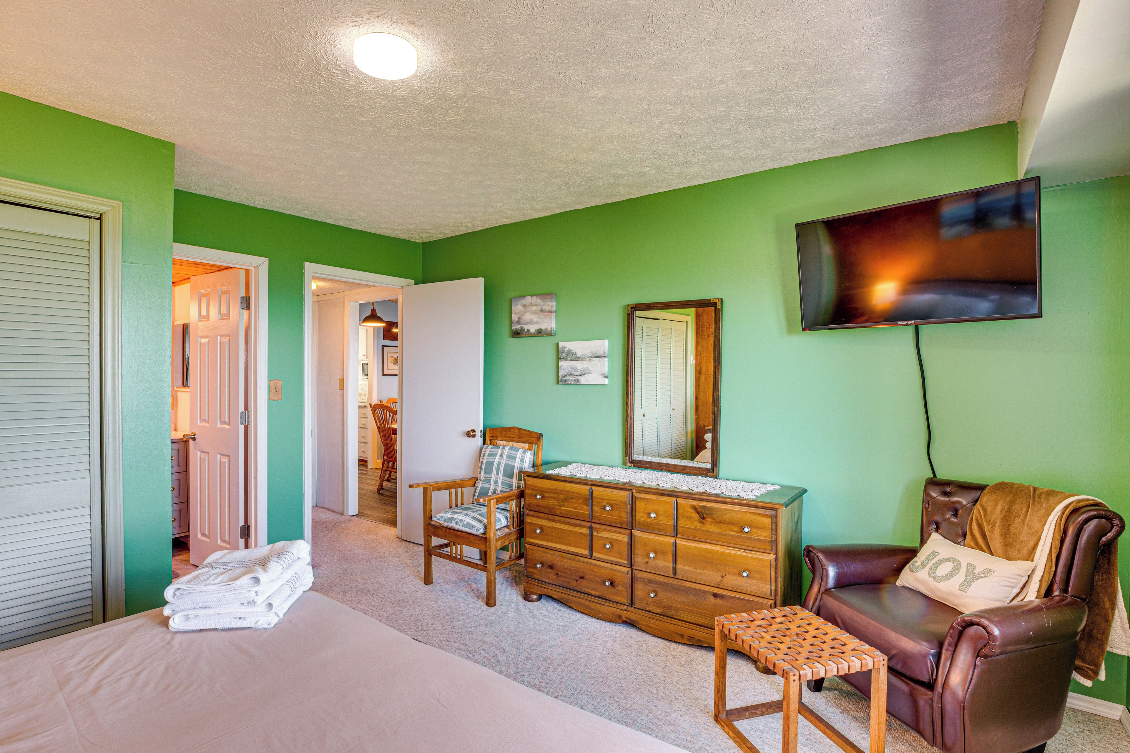 Un dormitorio con cama, cómoda, silla, sillón de cuero y televisor en la pared.