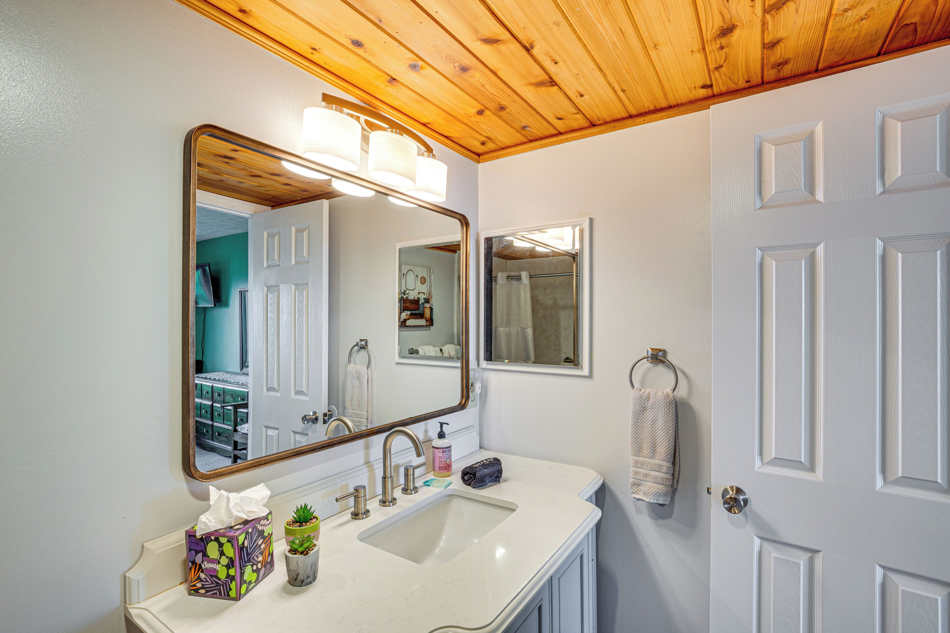 A bathroom with a white sink, a large mirror, and a wooden ceiling.