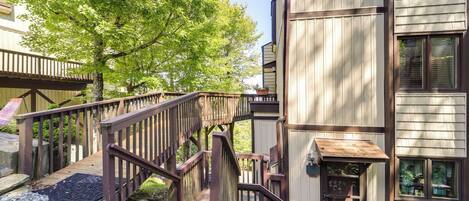 A wooden staircase leading to a building with a balcony, surrounded by trees.