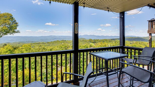 A balcony with a table and chairs, overlooking a lush landscape with mountains in the distance. - Hike, Ski & Fish! Sunset-view Condo in Beech Mtn (Banner Elk)