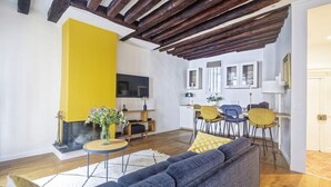 Ein Wohnzimmer mit grauem Sofa, gelber Akzentwand, Holzbalken, Kamin und Essbereich mit gelben Stühlen.