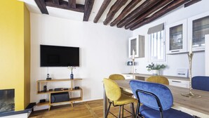 Ein modernes Wohnzimmer mit Holzboden, einem Flachbildfernseher, einem HolztV-Möbel, einem Esstisch mit Stühlen und einem Kamin.