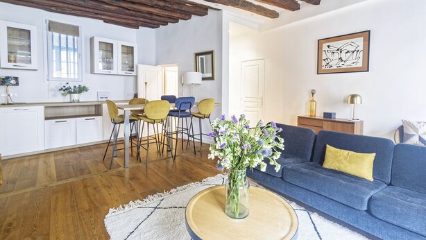 Ein modernes Wohnzimmer mit blauem Sofa, Esstisch aus Holz und Stühlen.