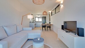 Un salon moderne comprenant un canapé, une table basse, un téléviseur et un coin repas avec des chaises et une table.
