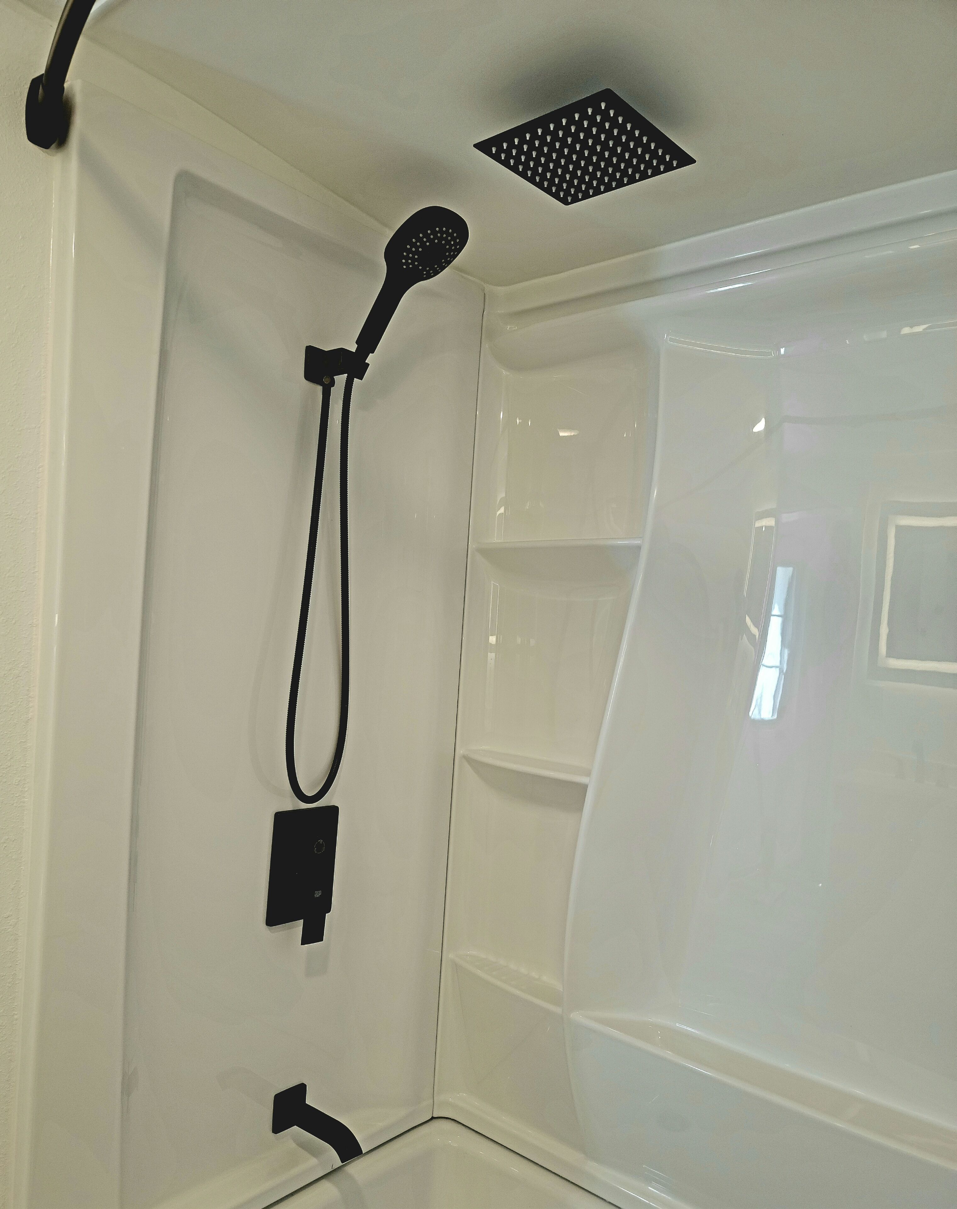 Ein Eckbereich eines Badezimmers mit Dusche, einer Handbrause und einer an der Wand montierten Bedienkonsole.
