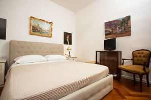 Ein Schlafzimmer mit einem großen Bett, einem Sessel, einem Fernseher auf einem Schrank und zwei gerahmten Bildern an der Wand.