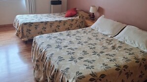 Ein Zimmer mit zwei Betten, Holzboden, einem fenster mit Vorhängen und einer Lampe auf einem Nachttisch.