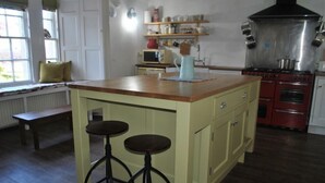 Uma cozinha com uma ilha central, banquetas, micro-ondas, prateleiras com potes, chaleira e fogão.