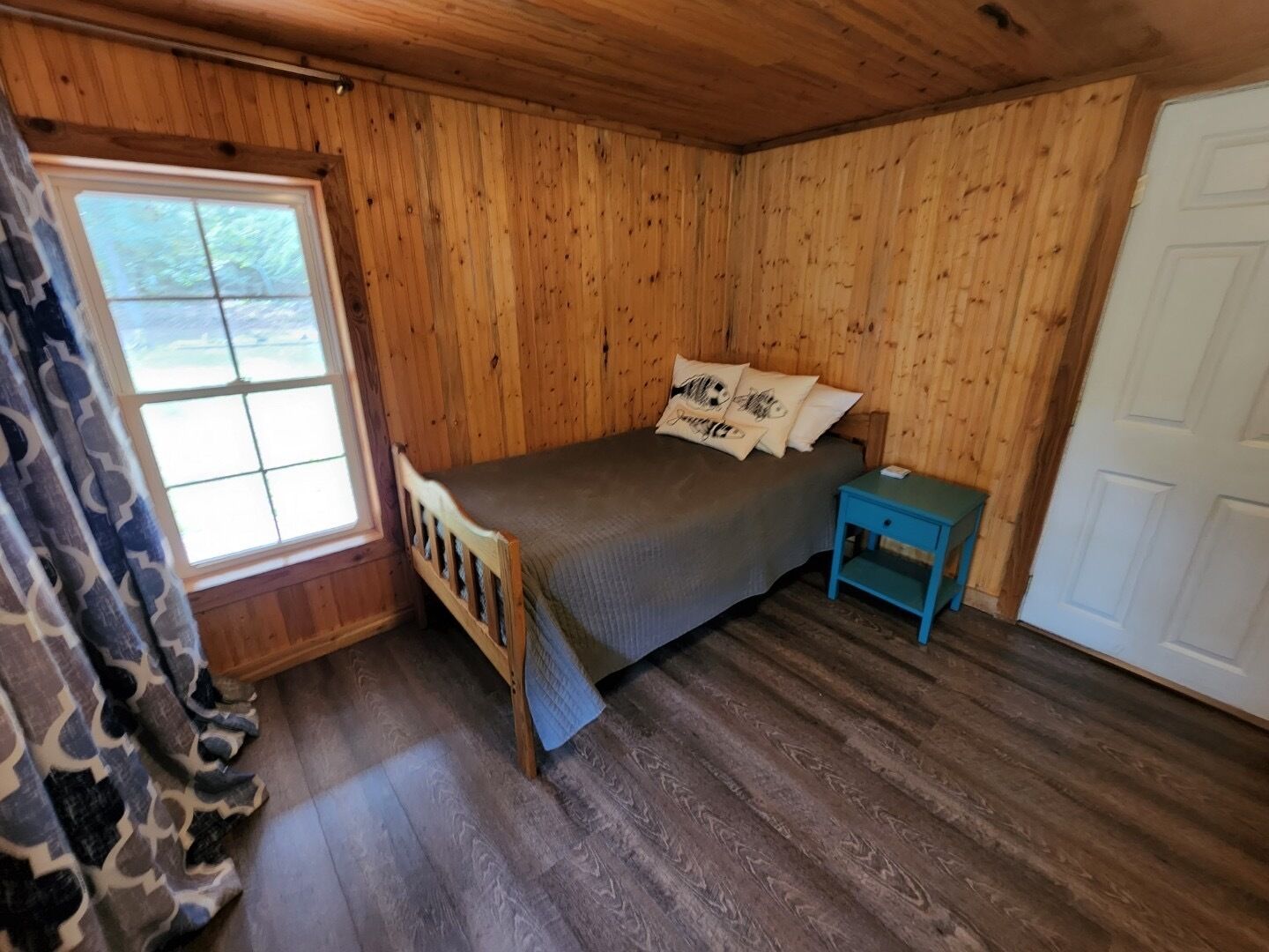 A wooden room with a bed, a window, and a door.