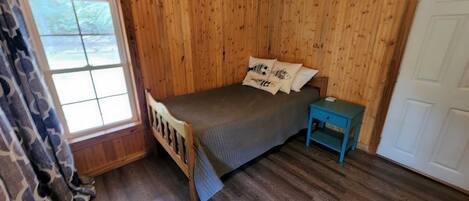 A wooden room with a bed, a window, and a door.