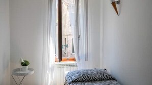 A bedroom with a bed, a window with curtains, a small table with a plant, and a radiator. - In the Art Quartier (Venezia)