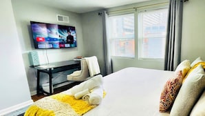 A hotel room with a large bed, a desk with a computer, a TV mounted on the wall, and a window with curtains.