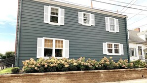 A two-story house with white shutters on the windows, a brick foundation, and a landscaped garden in front. - Charming Hydrangea Cottage in Sewickley Village 4bd/1.5 b - 20 min to Pittsburgh (Sewickley)