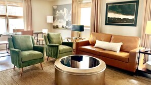 A living room with a green armchair, a brown sofa, a round coffee table, and a painting of clouds on the wall. - Charming Hydrangea Cottage in Sewickley Village 4bd/1.5 b - 20 min to Pittsburgh (Sewickley)