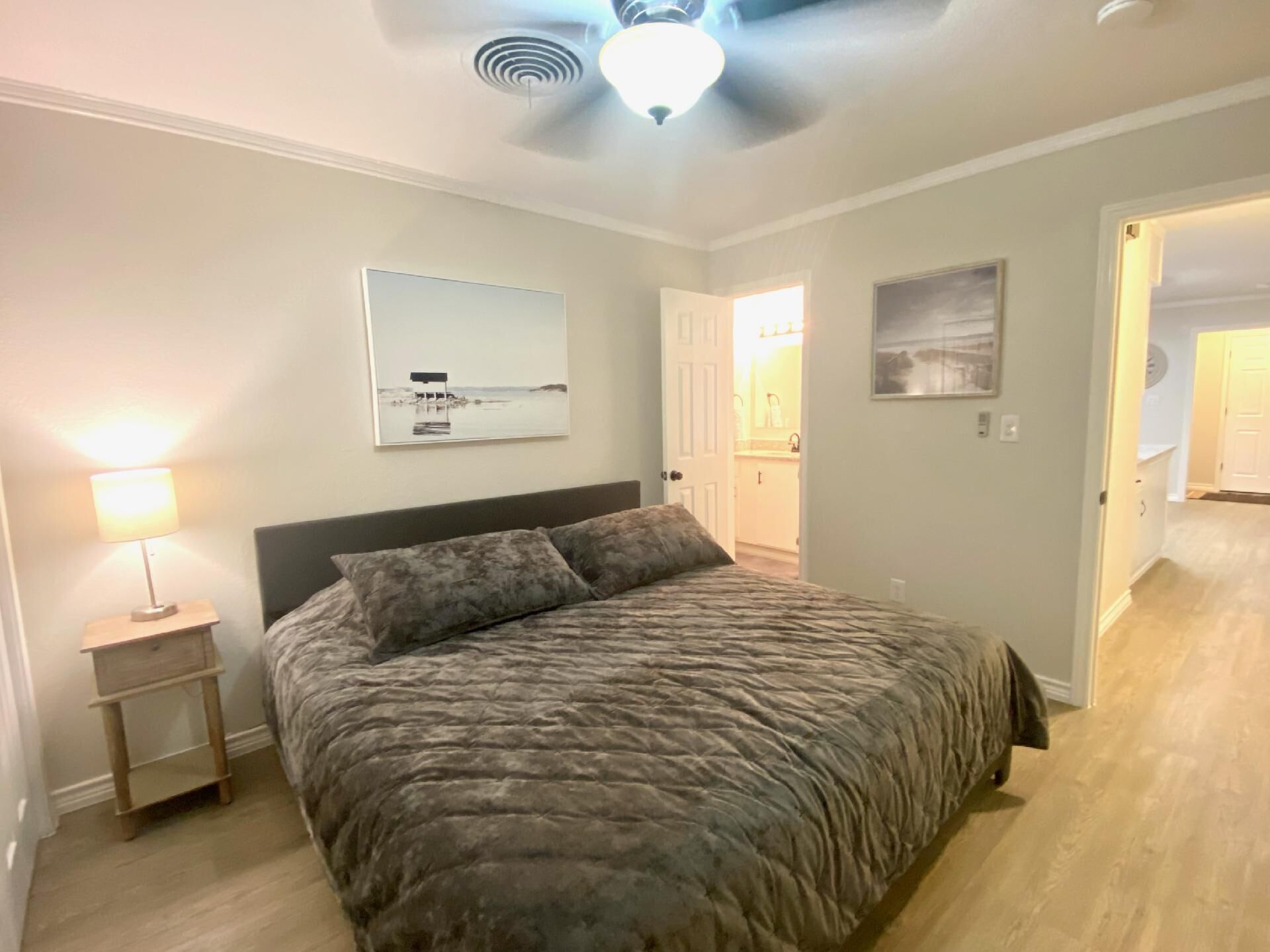 Un dormitorio con una cama, una mesita de noche, un ventilador de techo y obras de arte en las paredes.