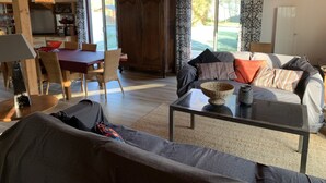 Ein gemütliches Wohnzimmer mit Holzboden, einem Essbereich mit Tisch und Stühlen, einer Couch mit Kissen und einem großen Fenster mit Vorhängen.