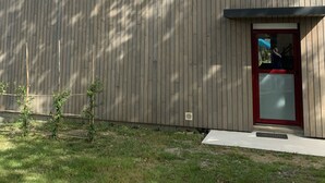 Ein modernes Gebäude mit Holzfassade, zwei Fenstern mit roten Rahmen und einer roten Tür.