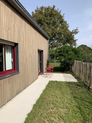 Un bâtiment moderne avec une façade en bois, un patio en béton et une porte à cadre rouge.