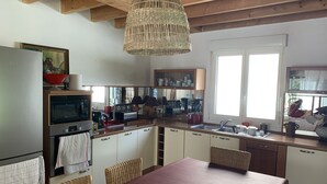 Eine Küche mit Holzbalkendecke, einem Esstisch, Korbstühlen und einer Pendelleuchte.