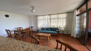 Un salon comprenant un canapé, des fauteuils, une table basse, une table à manger et un ventilateur de plafond.