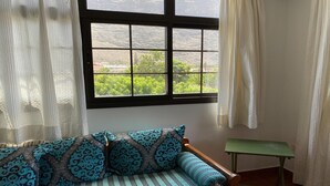 Una habitación con ventana, un sofá con cojines estampados, una mesita y cortinas de gasa.