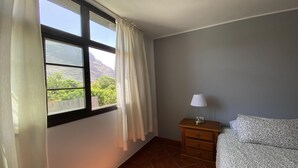 Una habitación con cama, mesita de noche, lámpara y ventana con cortinas.